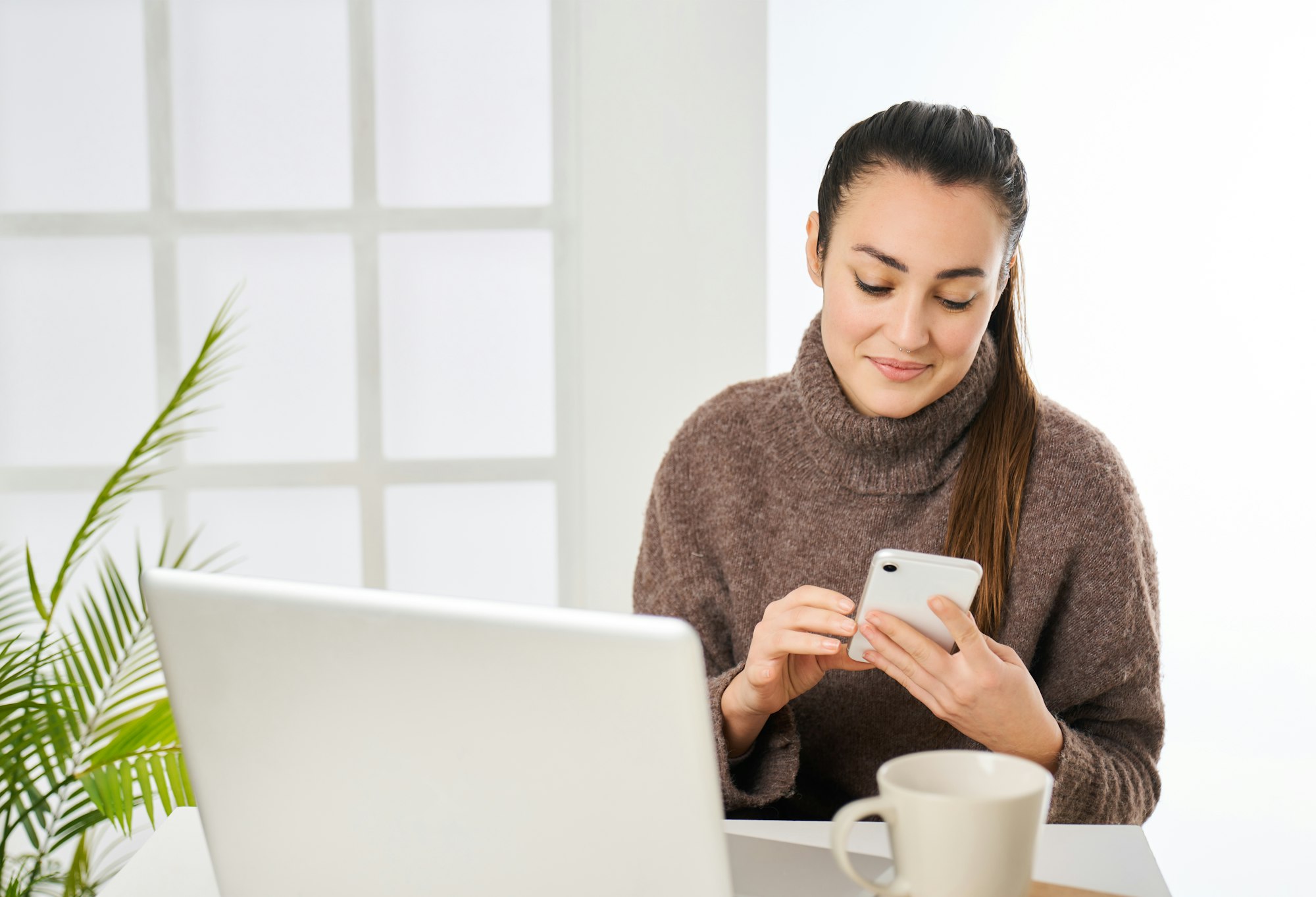 a woman working at the computer and looking at the messages on the phone from the office
